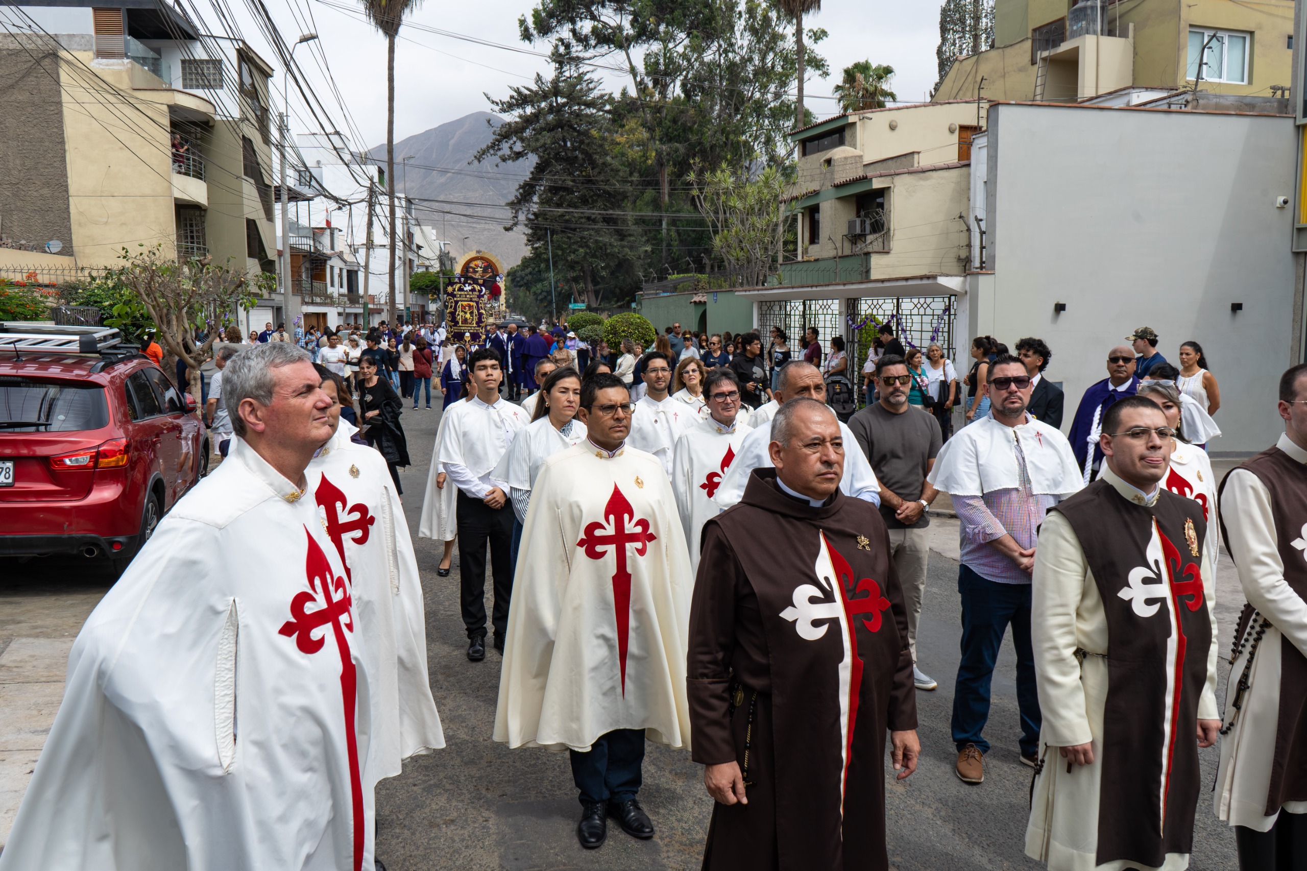 Des Hérauts de l'Évangile en habit marchent en procession dans une rue de Lima, suivis par les fidèles et le brancard du Seigneur des Miracles
