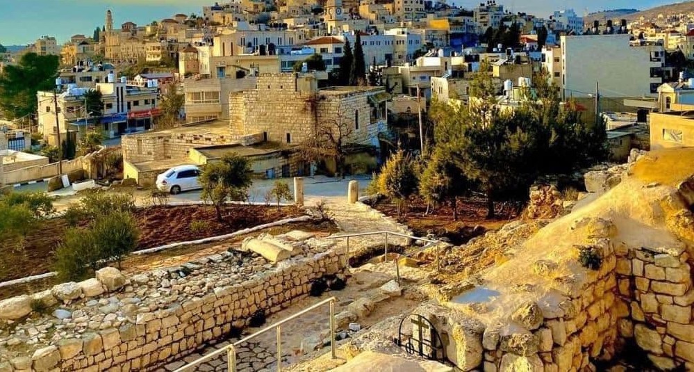 Vue du village de Taybeh, en Cisjordanie, avec ses maisons de pierre claire, des oliviers et des ruines antiques au premier plan